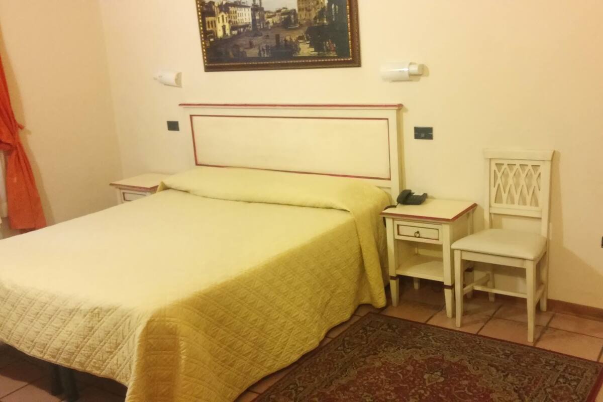 A bedroom with a bed, bedside table, chair, and a painting on the wall.