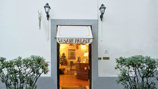 The entrance to VASARI PALACE with a sign above the door, potted plants on either side, and a Christmas tree inside. - Hotel Vasari (Florence)