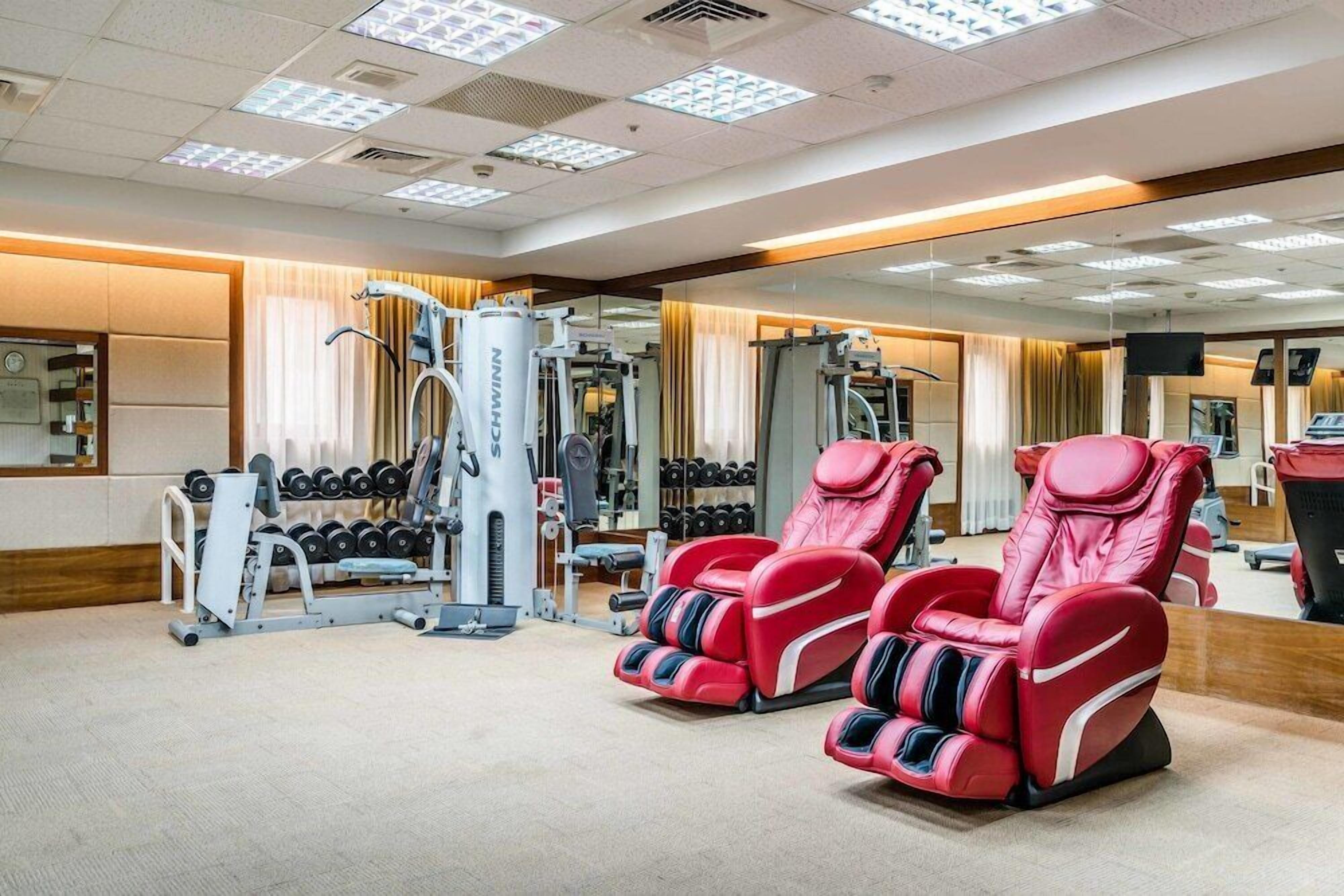 Un gimnasio con equipo de ejercicio, un espejo y sillones de masaje rojos.