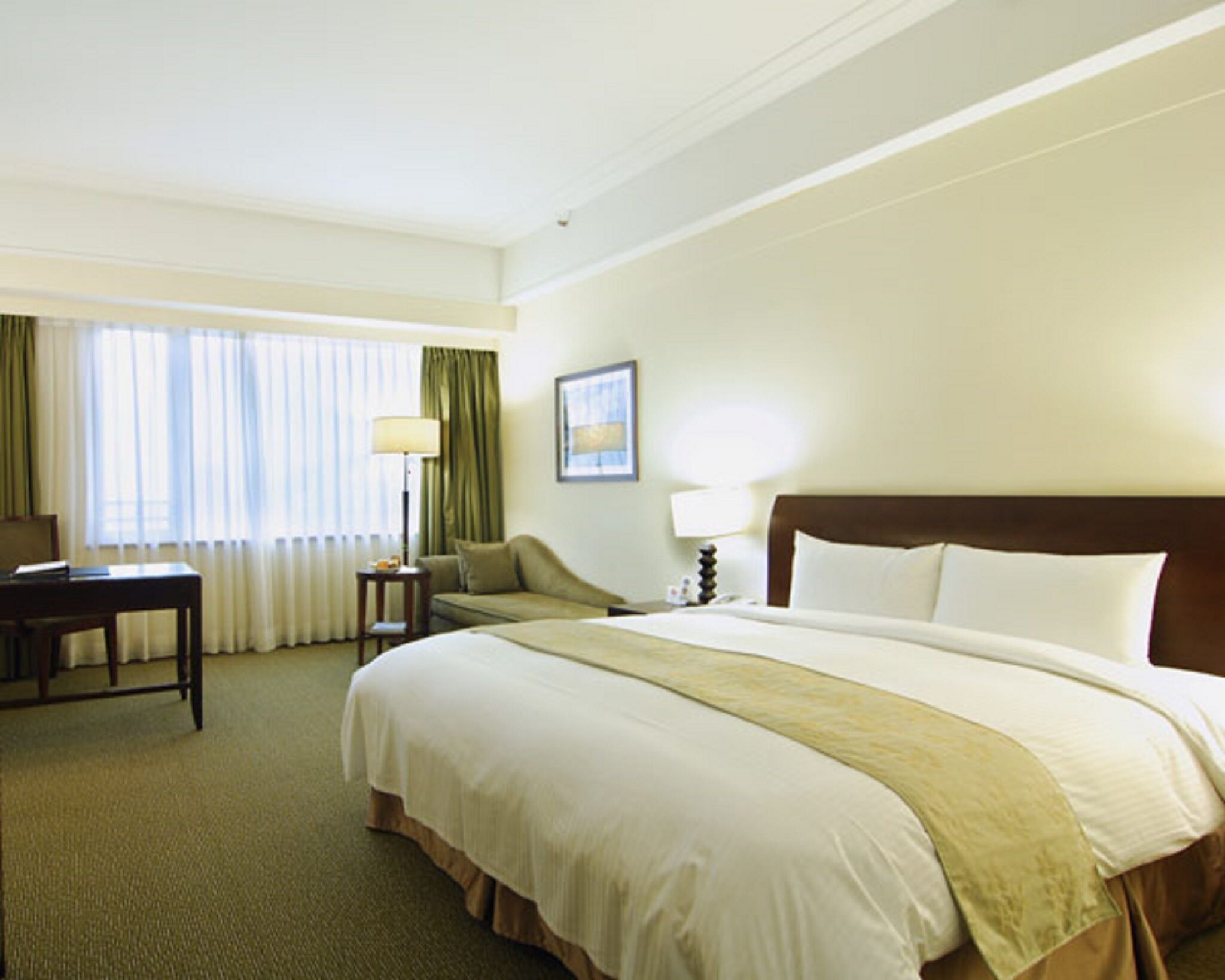 A hotel room with a large bed, a desk, a chair, a lamp, and a window with curtains.