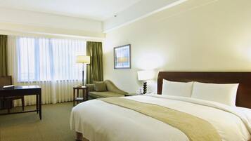 Una habitación de hotel con una cama grande, un escritorio, una silla, una lámpara y un ventanal con cortinas.