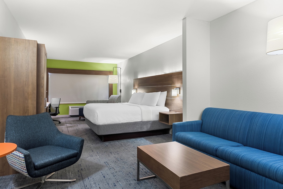 A hotel room with a bed, a blue sofa, a wooden coffee table, a chair, and a desk.