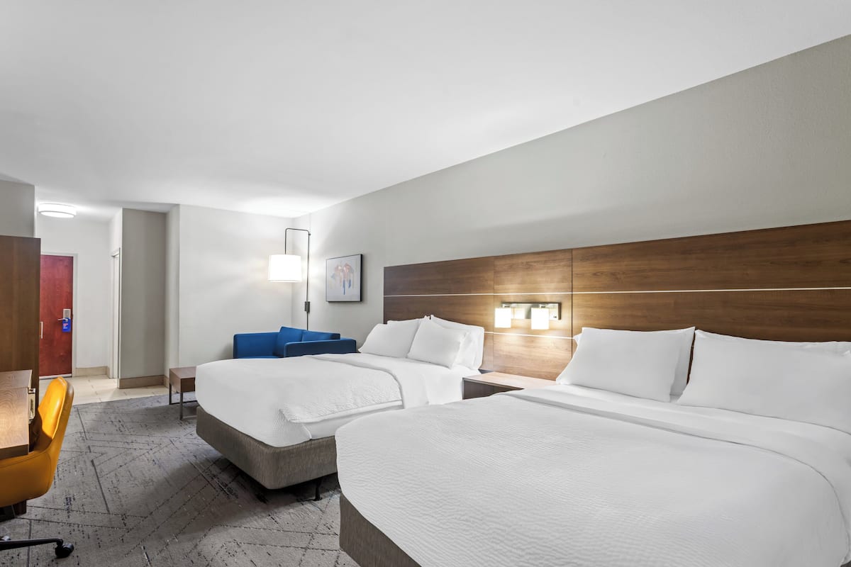 A hotel room with two beds, a desk, a chair, and a nightstand with lamps.