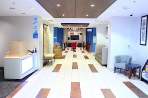 Un hall d’hôtel comprenant un comptoir d’accueil, un espace détente avec des chaises et des tables, un mur bleu orné d’une enseigne et un sol à motifs.