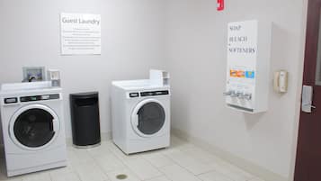 A guest laundry area with two washing machines, a trash bin, and a sign listing available laundry supplies.