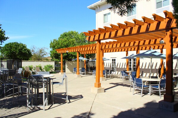 Un espace extérieur aménagé en terrasse, avec des tables et des chaises, une pergola et des parasols pour créer de l’ombre.