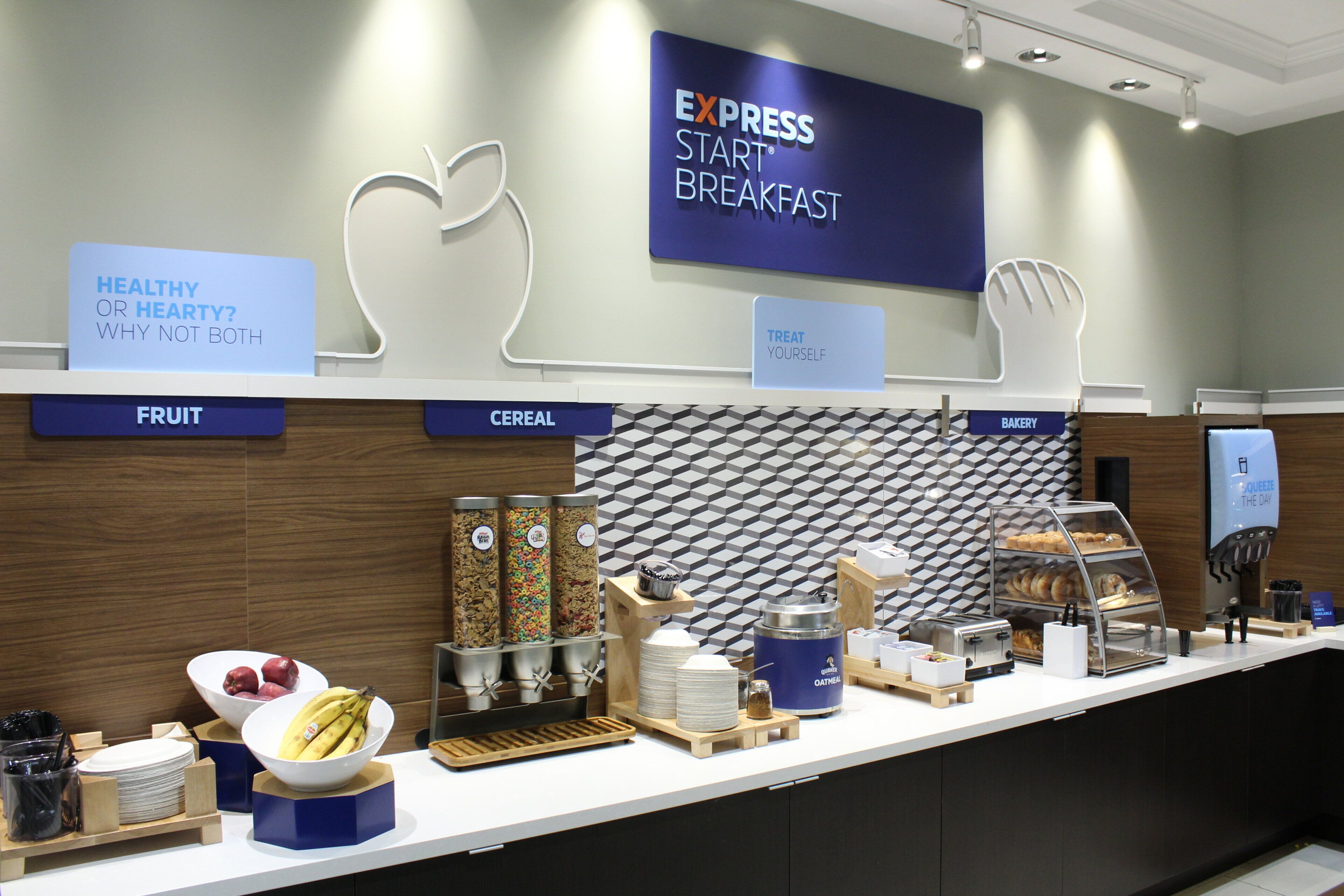 Ein Frühstücksbuffet mit beschrifteten Bereichen für Obst, Müsli und Backwaren, sowie ein Schild, das eine gesunde Frühstücksoption bewirbt.