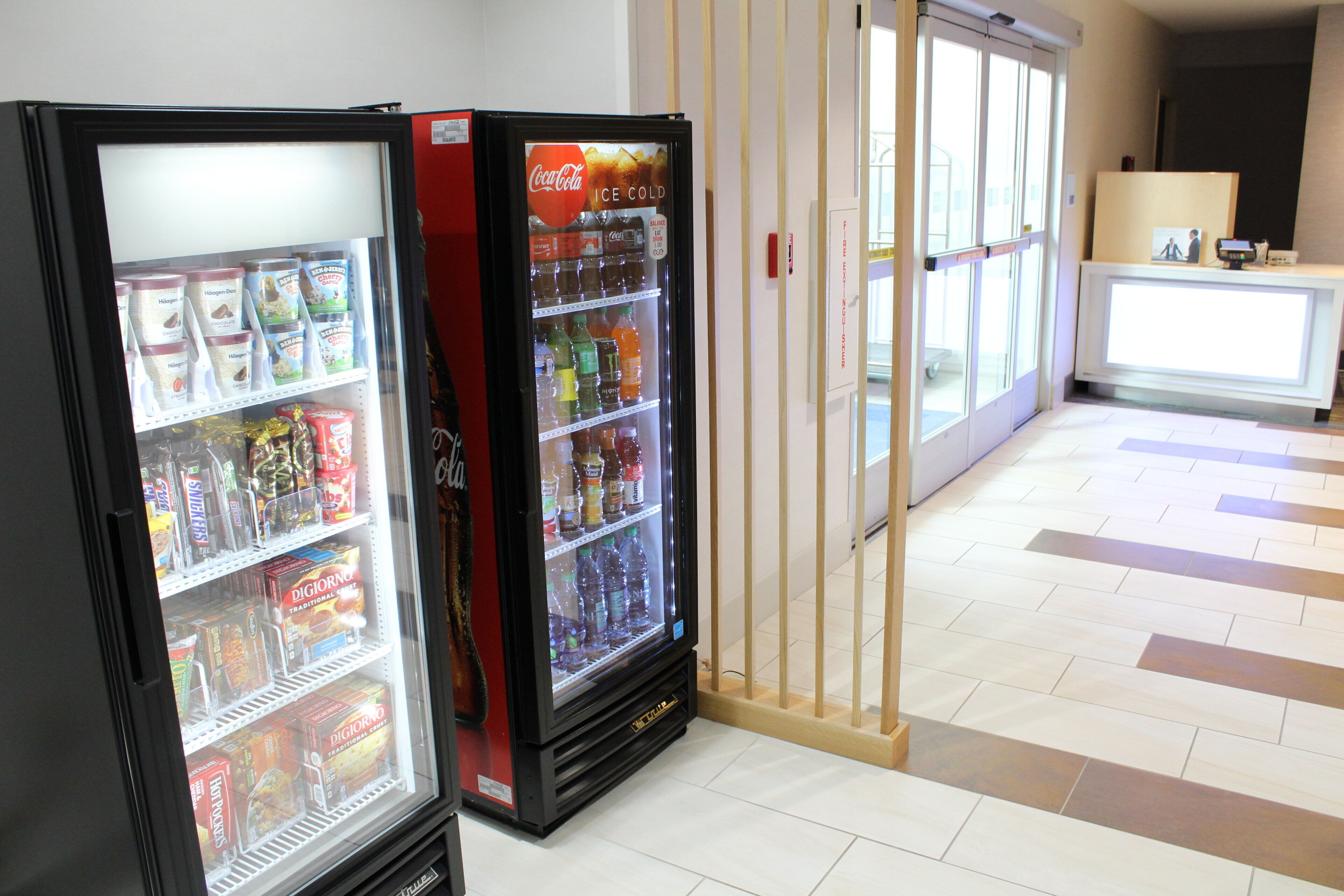 Two beverage dispensers in a hotel lobby with a tiled floor and a reception desk in the background.