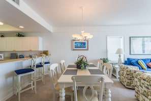 A dining area with a white table, blue cushioned chairs, and a chandelier.