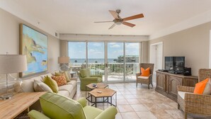 A spacious living room with a large window, a ceiling fan, and a view of the sea. - Hodnett Cooper St Simons Grand - 3 Bedroom (St. Simons Island)