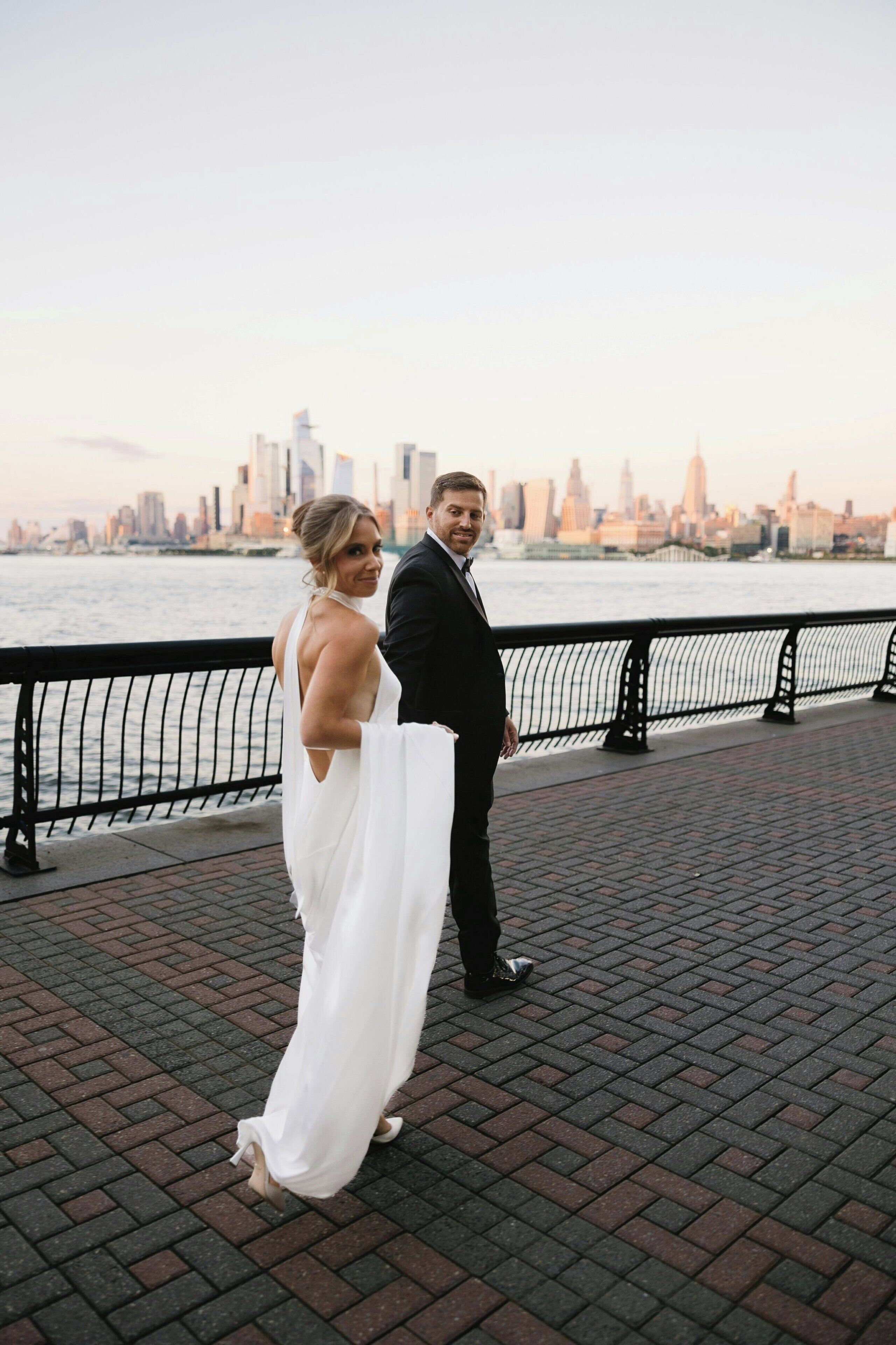 A couple standing on a brick-paved walkway with a city skyline in the background.