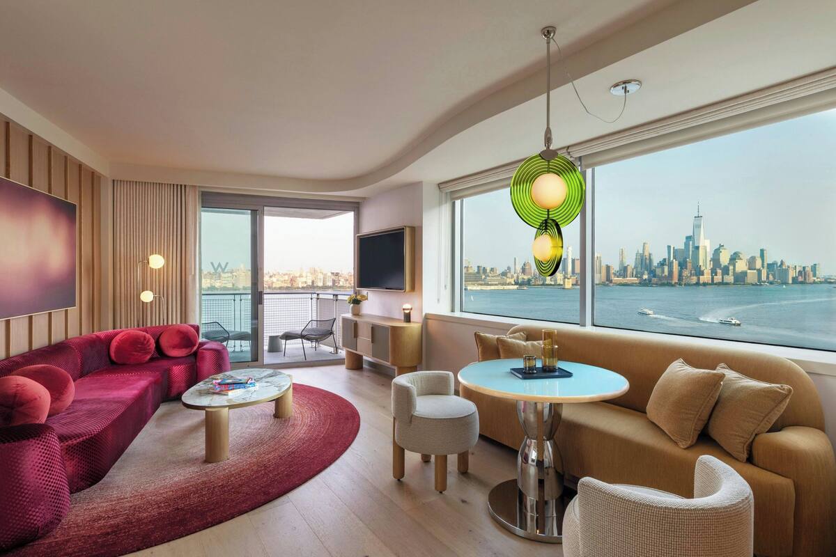 Un salón moderno con un amplio ventanal que ofrece vistas a un horizonte urbano y al agua.