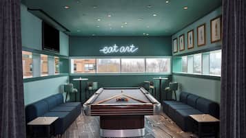 A pool table in a room with teal walls, a neon 'eat art' sign, and framed pictures on the wall.