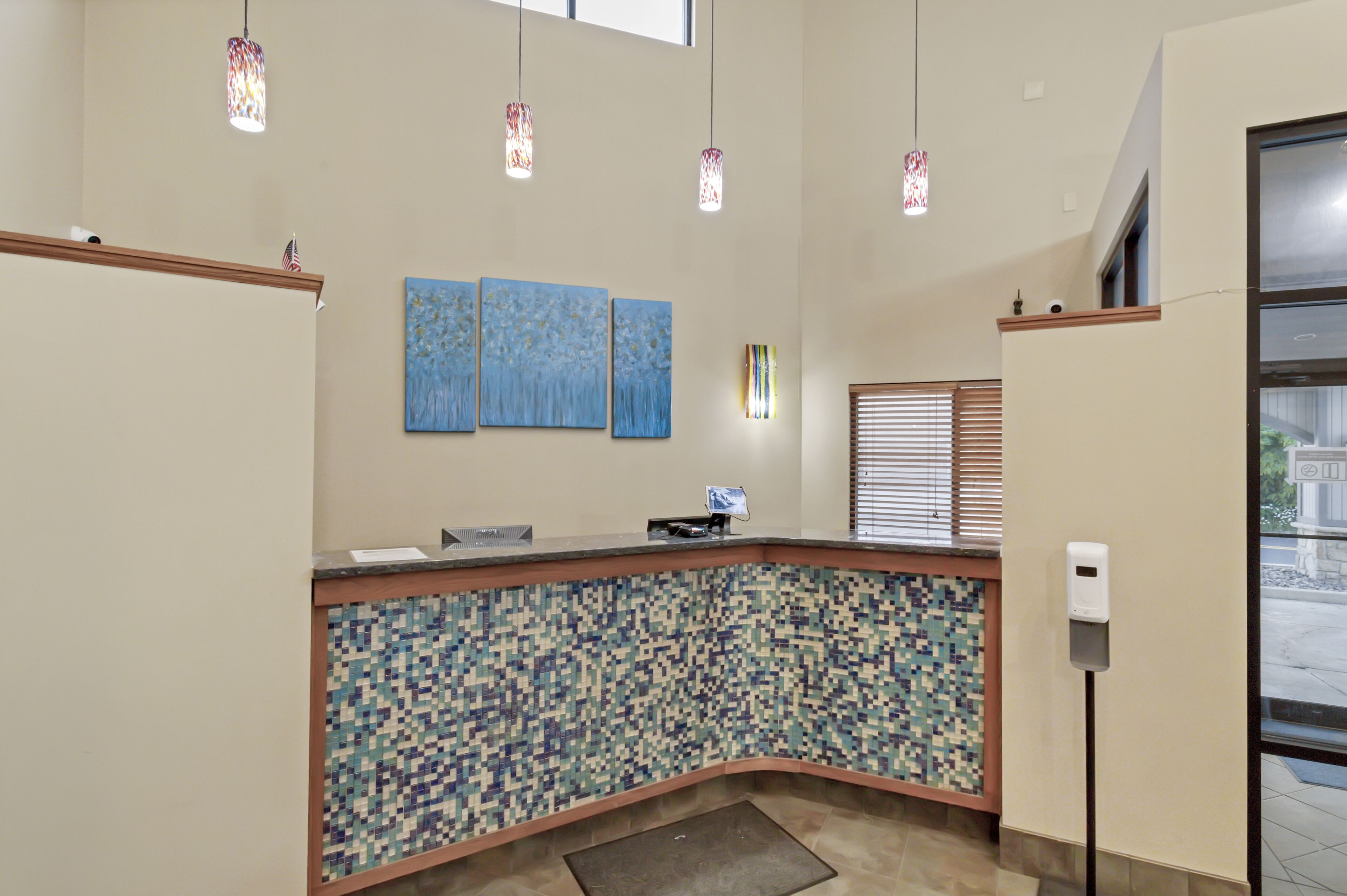 Un espace d’accueil doté d’un comptoir recouvert de mosaïques, de trois tableaux bleus et de luminaires suspendus.