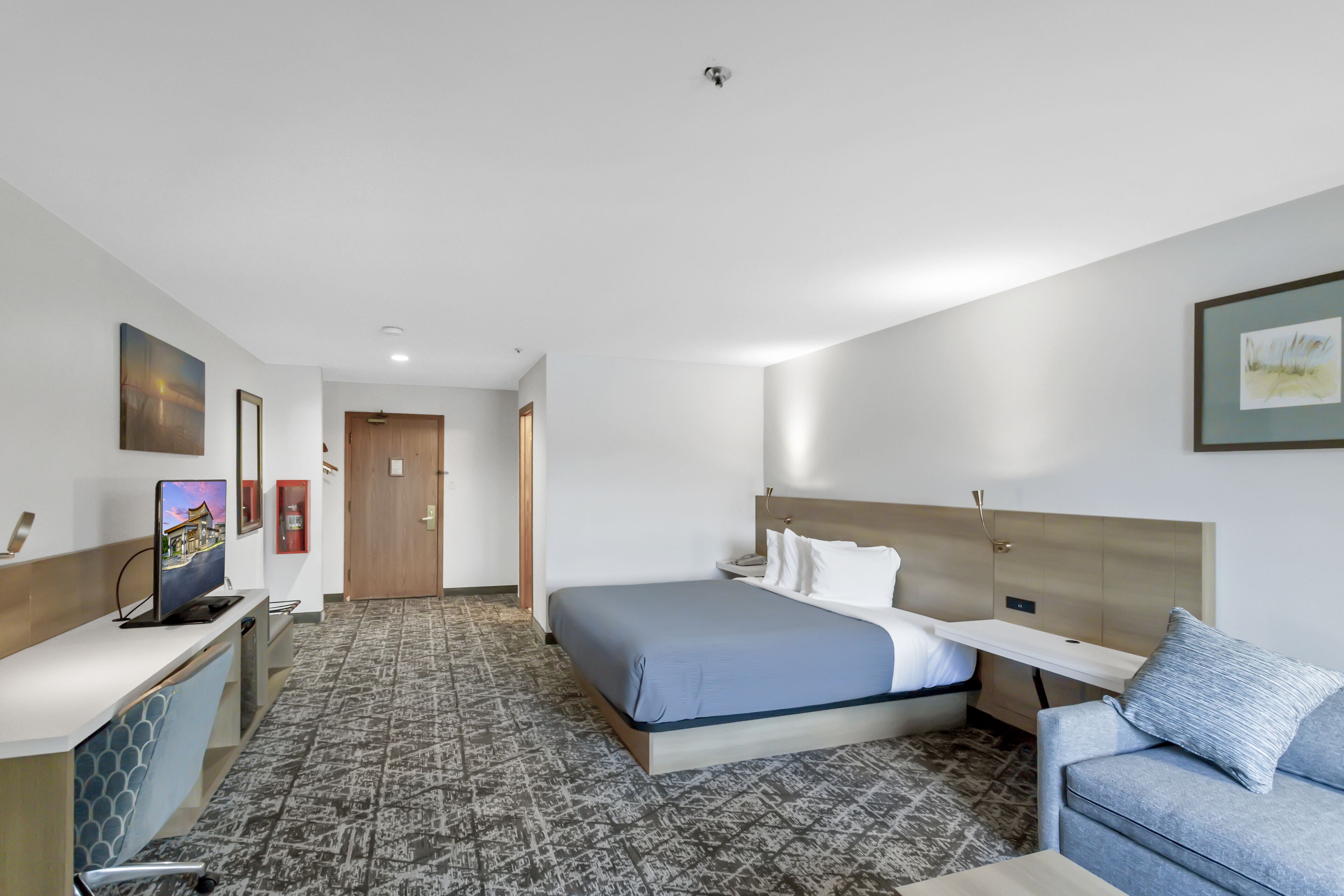 A hotel room with a bed, a desk, a chair, a TV, and a couch.