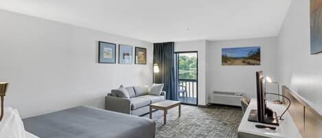 Habitación de hotel con cama, sofá, una mesita, escritorio con computadora y ventana con vistas a zonas verdes.