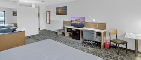 Ein Hotelzimmer mit Bett, Schreibtisch, Stuhl, Fernseher und Kunstwerk an der Wand.