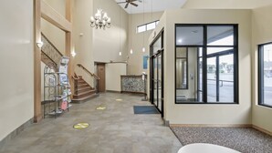 A spacious lobby with a staircase, a reception desk, and large windows offering a view of the outside. - Waterbird Lakeside Inn (Chesterton)