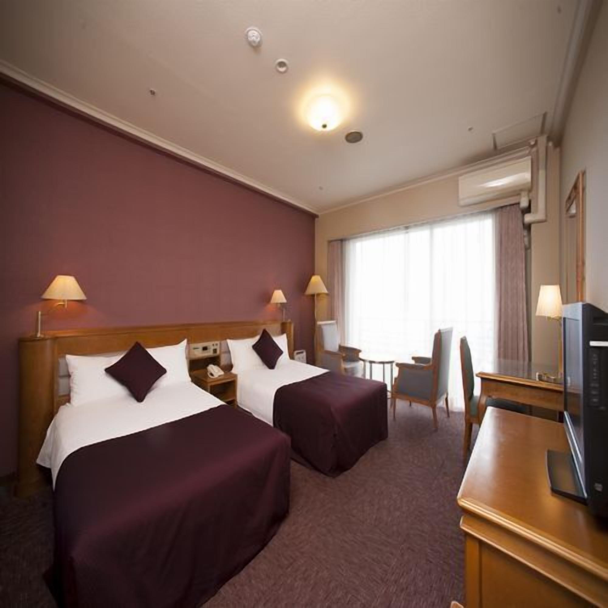 Une chambre d’hôtel avec deux lits, un bureau, une chaise, une télévision et une fenêtre avec des rideaux.