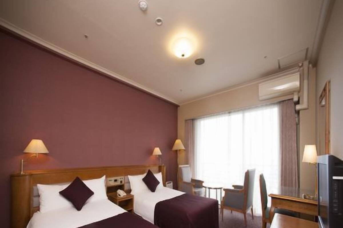 Une chambre d’hôtel avec deux lits, un bureau, une chaise, une télévision et une fenêtre avec des rideaux.