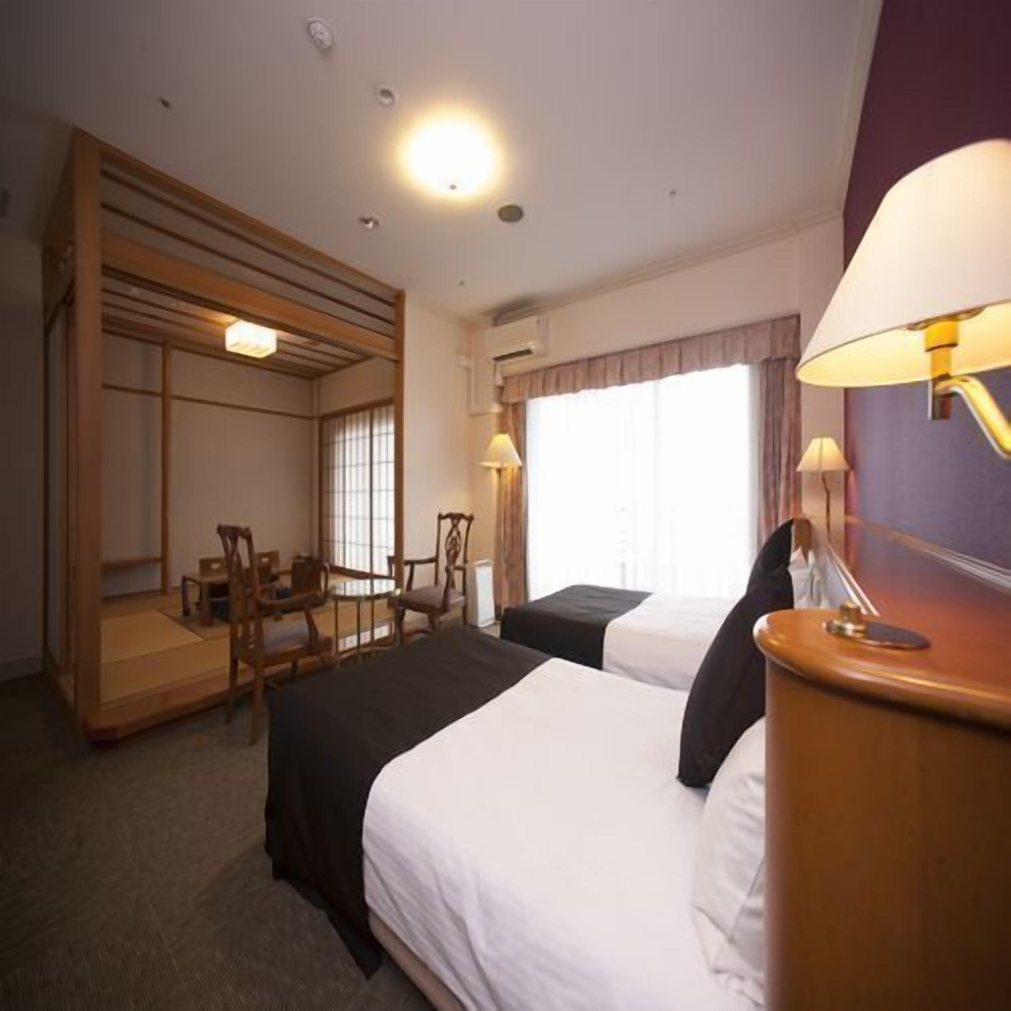 A hotel room with a bed, a desk, chairs, and a window.