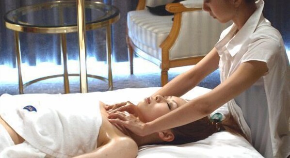 A person receiving a massage in a room with a bed, a round glass table, and a chair. - Sendai Hills Hotel (Sendai)