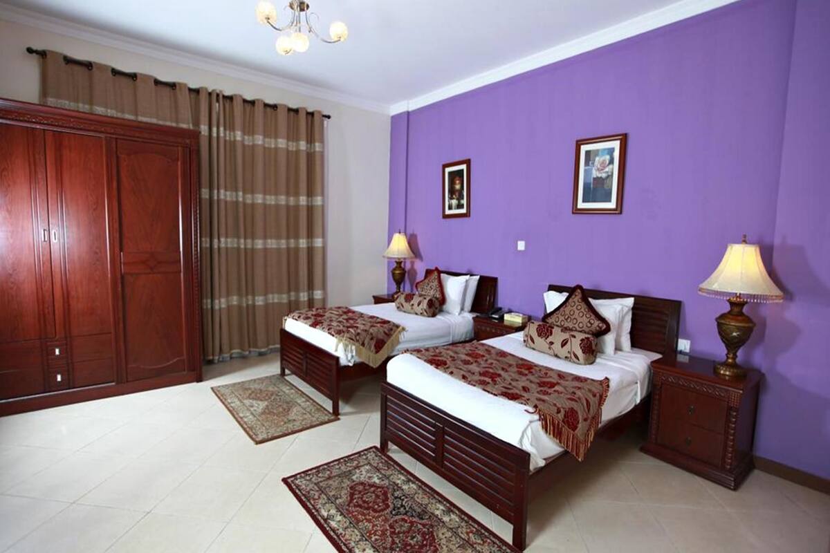 A room with two beds, a wardrobe, a chandelier, and a purple wall.