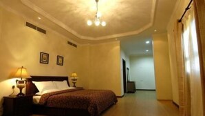 Habitación de hotel con una cama grande, dos lámparas de noche, una lámpara del techo y vista al pasillo.