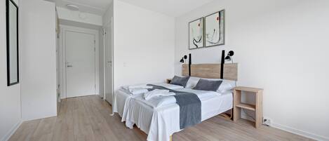 Una camera da letto con un letto grande, un comodino e una piccola scrivania. Si apre una porta verso un'altra stanza.
