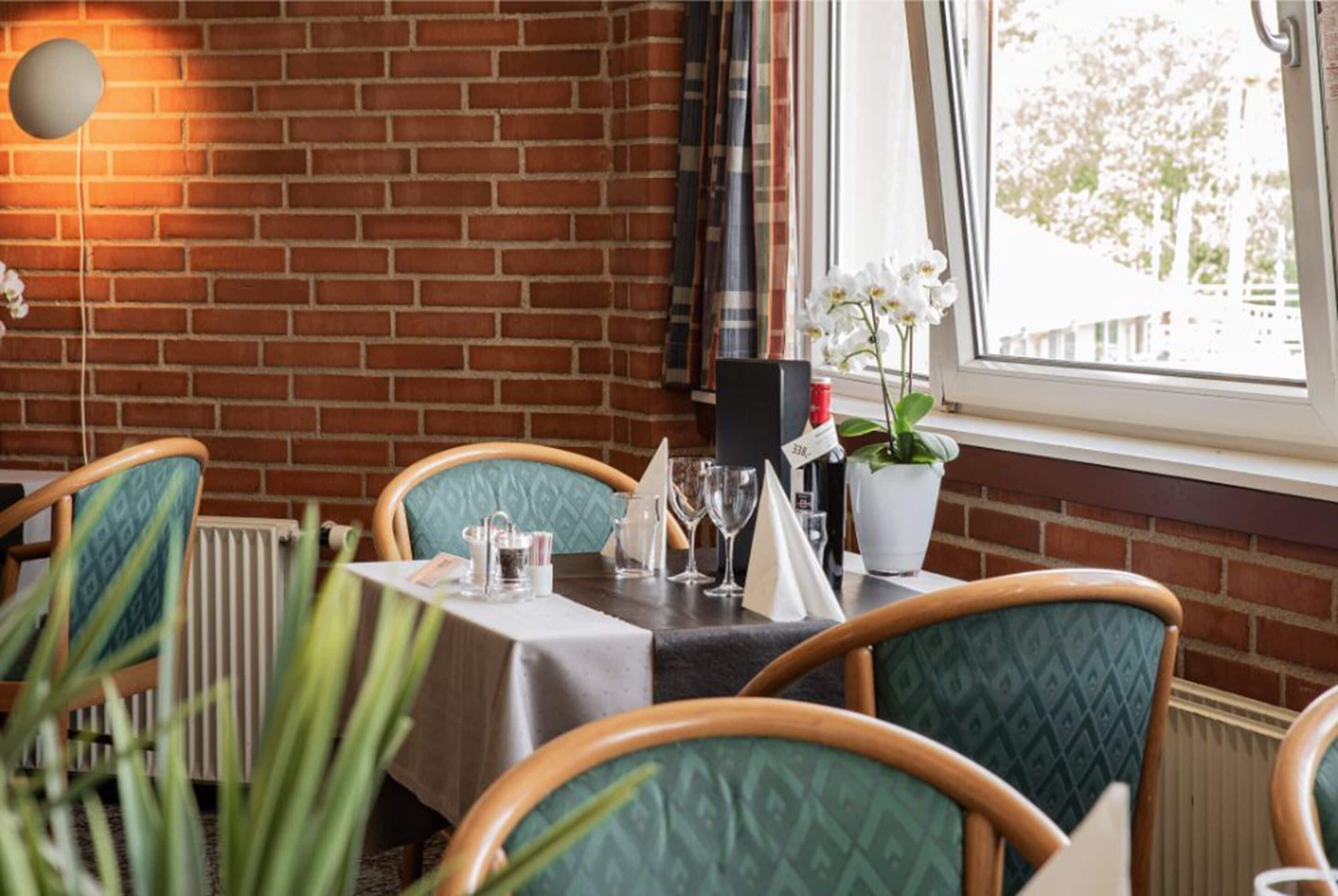 A restaurant with brick walls, green upholstered chairs, a table set with a white tablecloth, and a potted orchid.