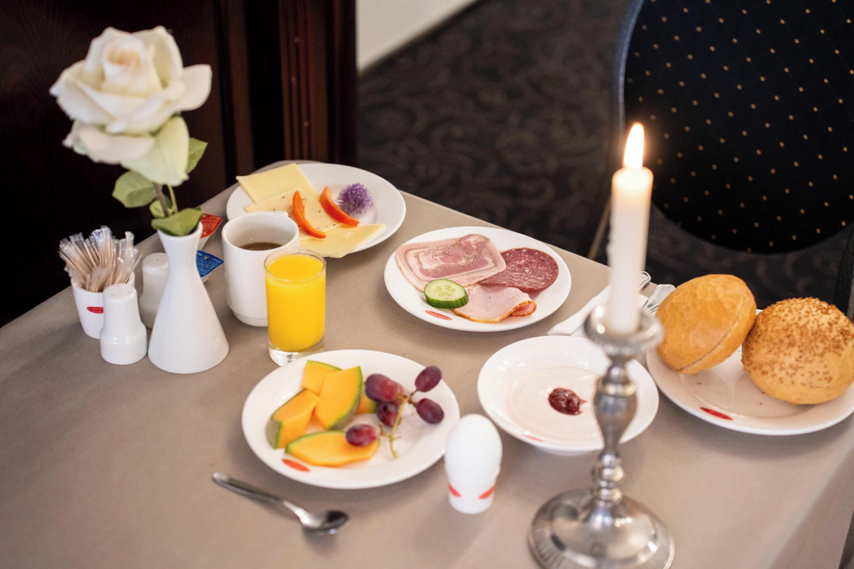 Una mesa de desayuno con platos de comida, una vela y una rosa.