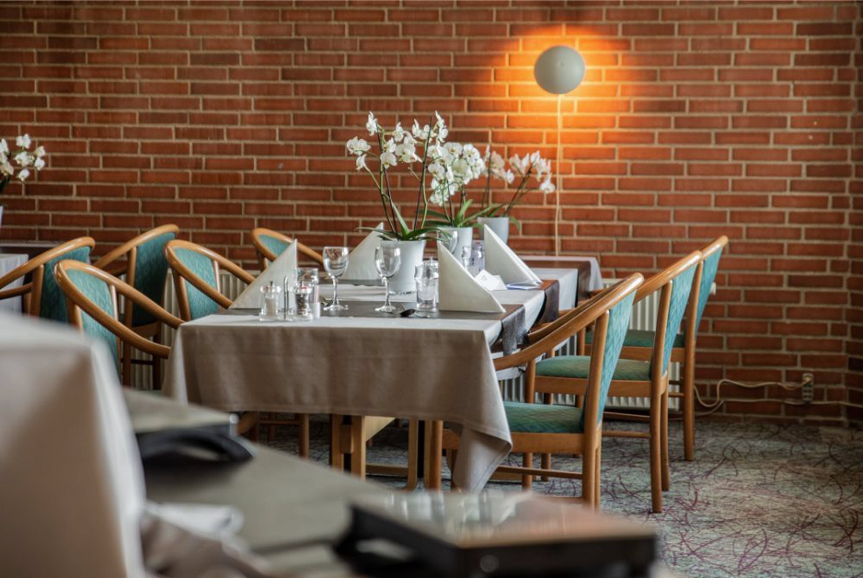 A restaurant with brick walls, wooden chairs, and a table set with white tablecloths and glassware.