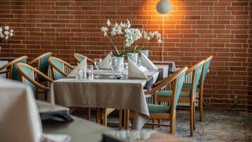 A restaurant with brick walls, wooden chairs, and a table set with white tablecloths and glassware.
