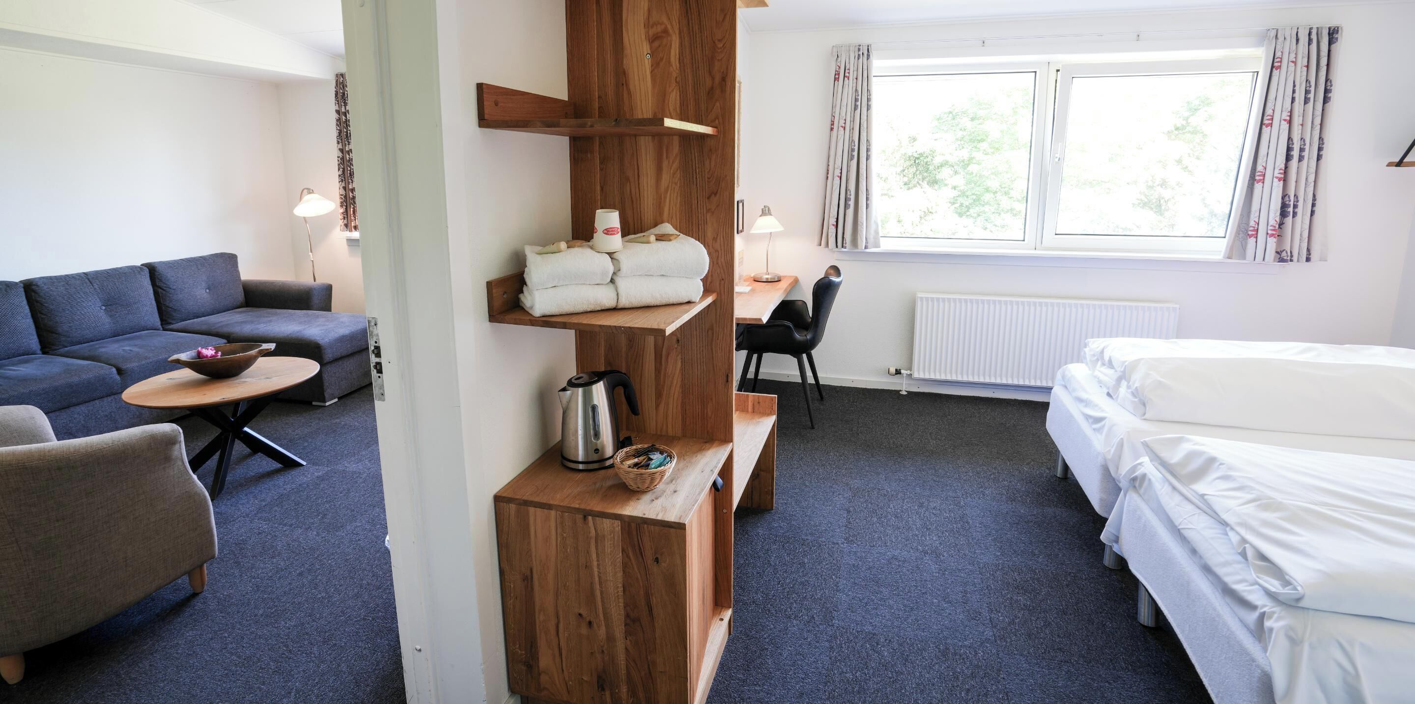Une chambre d’hôtel avec un canapé, un bureau et une chaise, un lit et une fenêtre avec des rideaux.