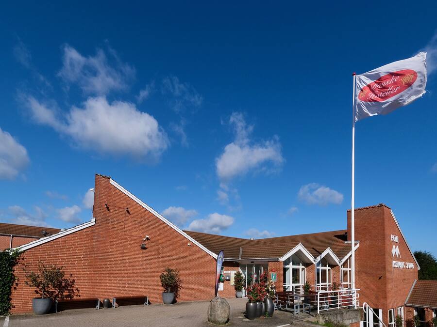 A hotel with a brick facade, a flagpole with a flag, and potted plants in the foreground.