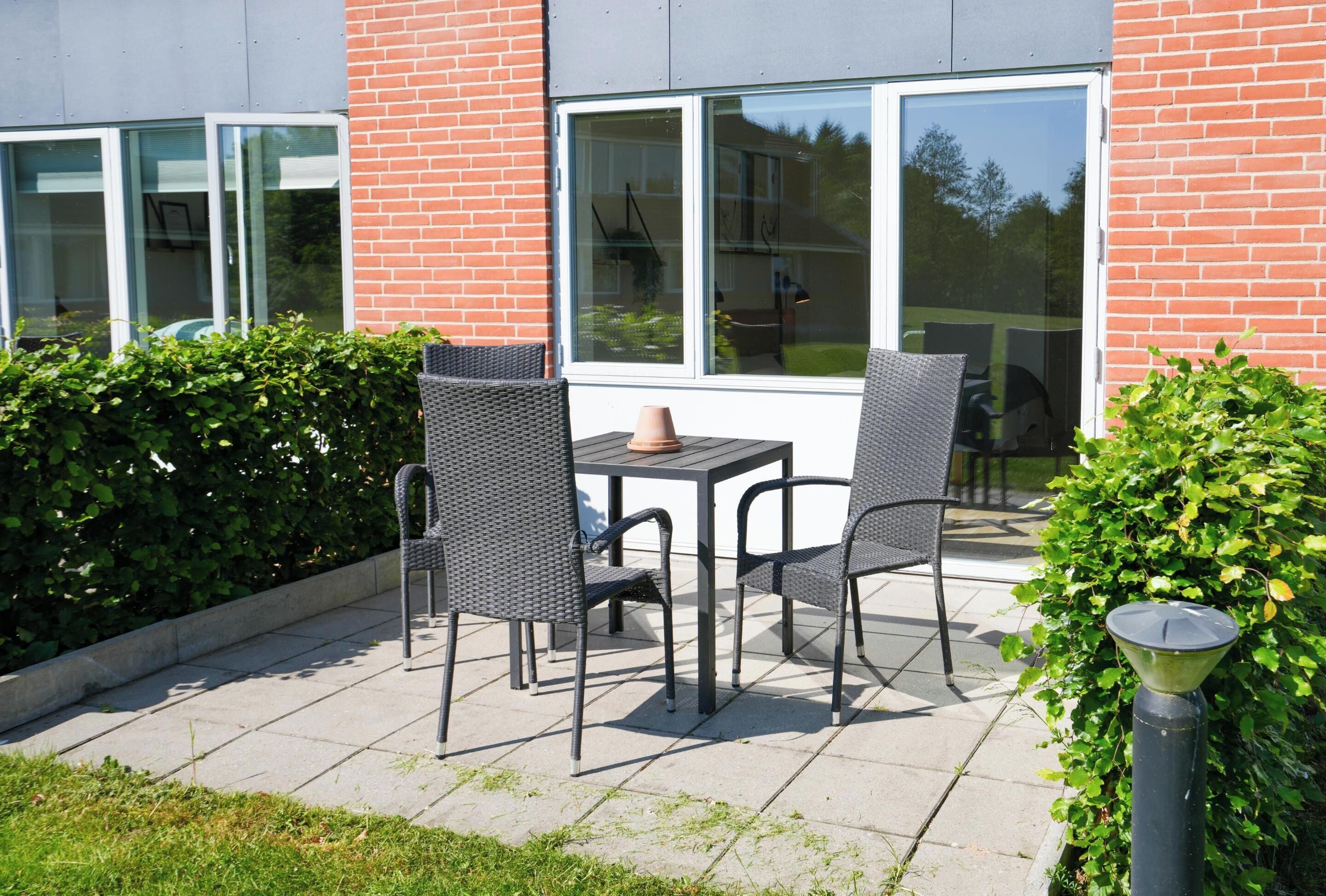 Een terras met twee stoelen, een tafel, een bakstenen muur en een raam.