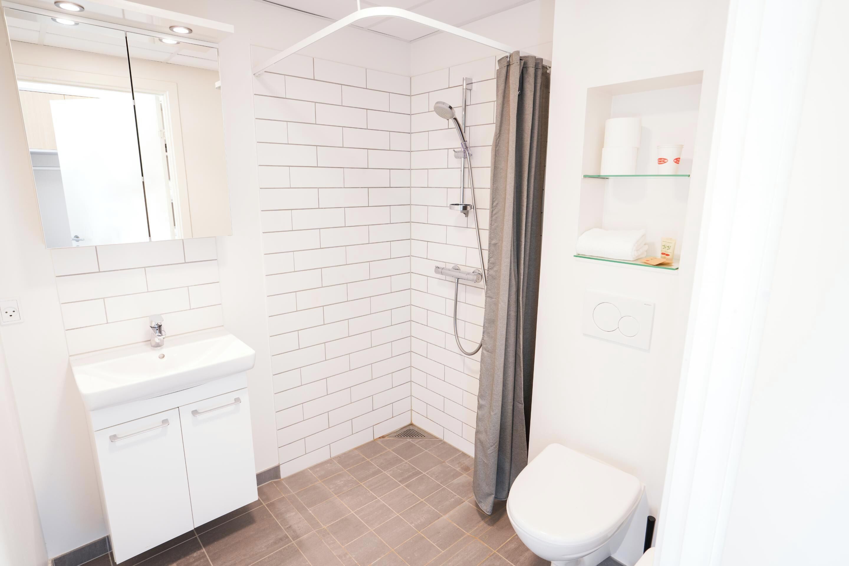 A bathroom with a white sink, mirror, shower, and toilet.