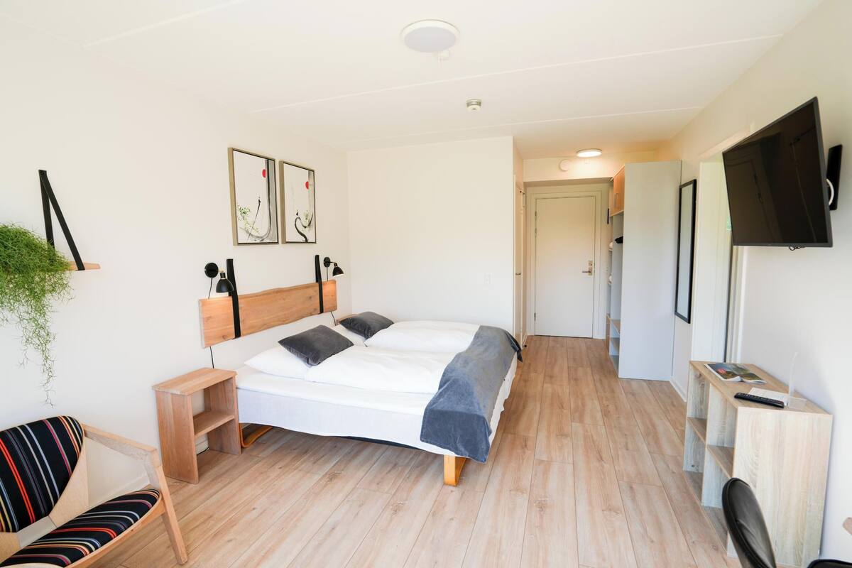 A modern bedroom with a bed, bedside tables, a TV, and a desk.
