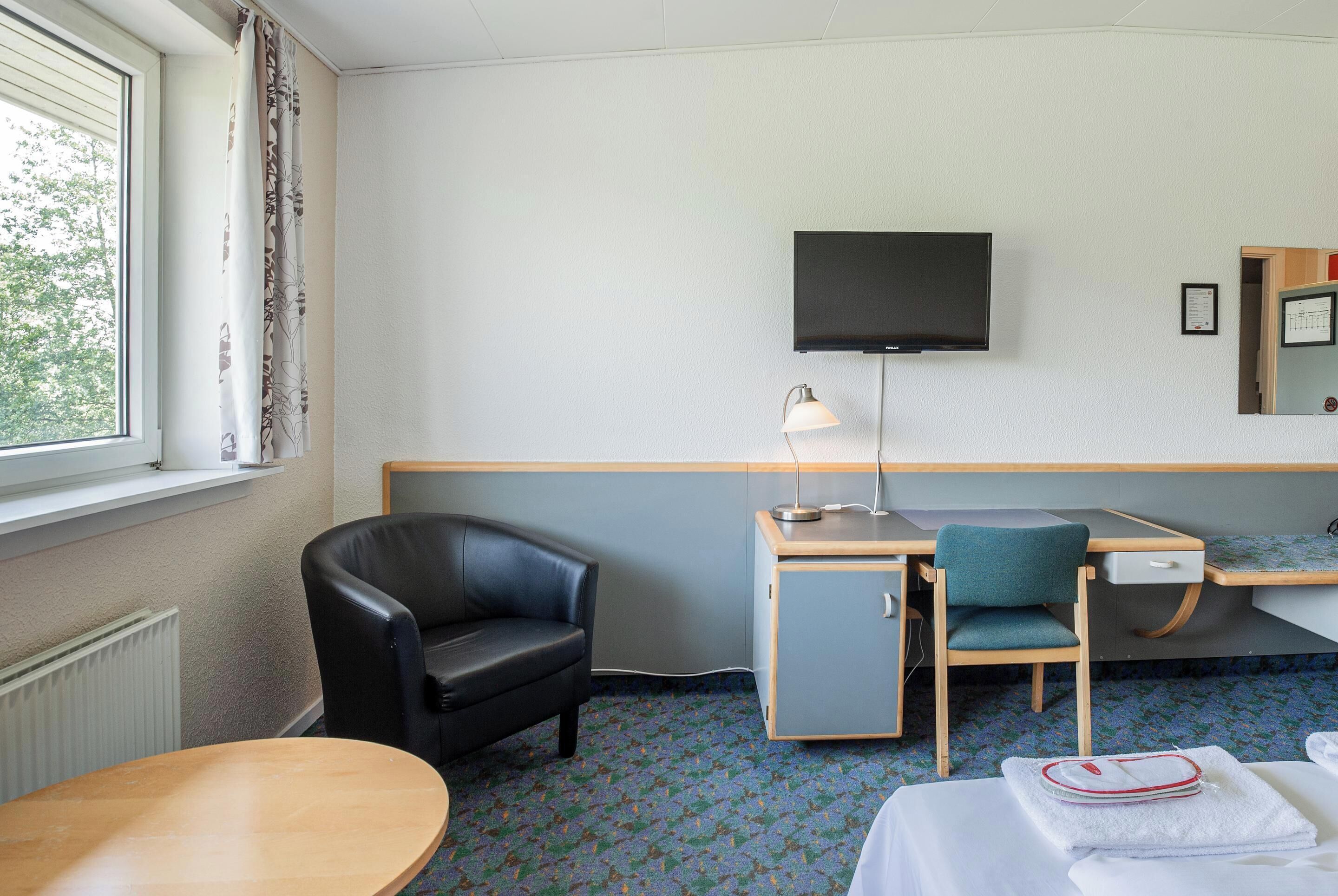 A hotel room with a desk, chair, TV, lamp, and a bed with a towel.
