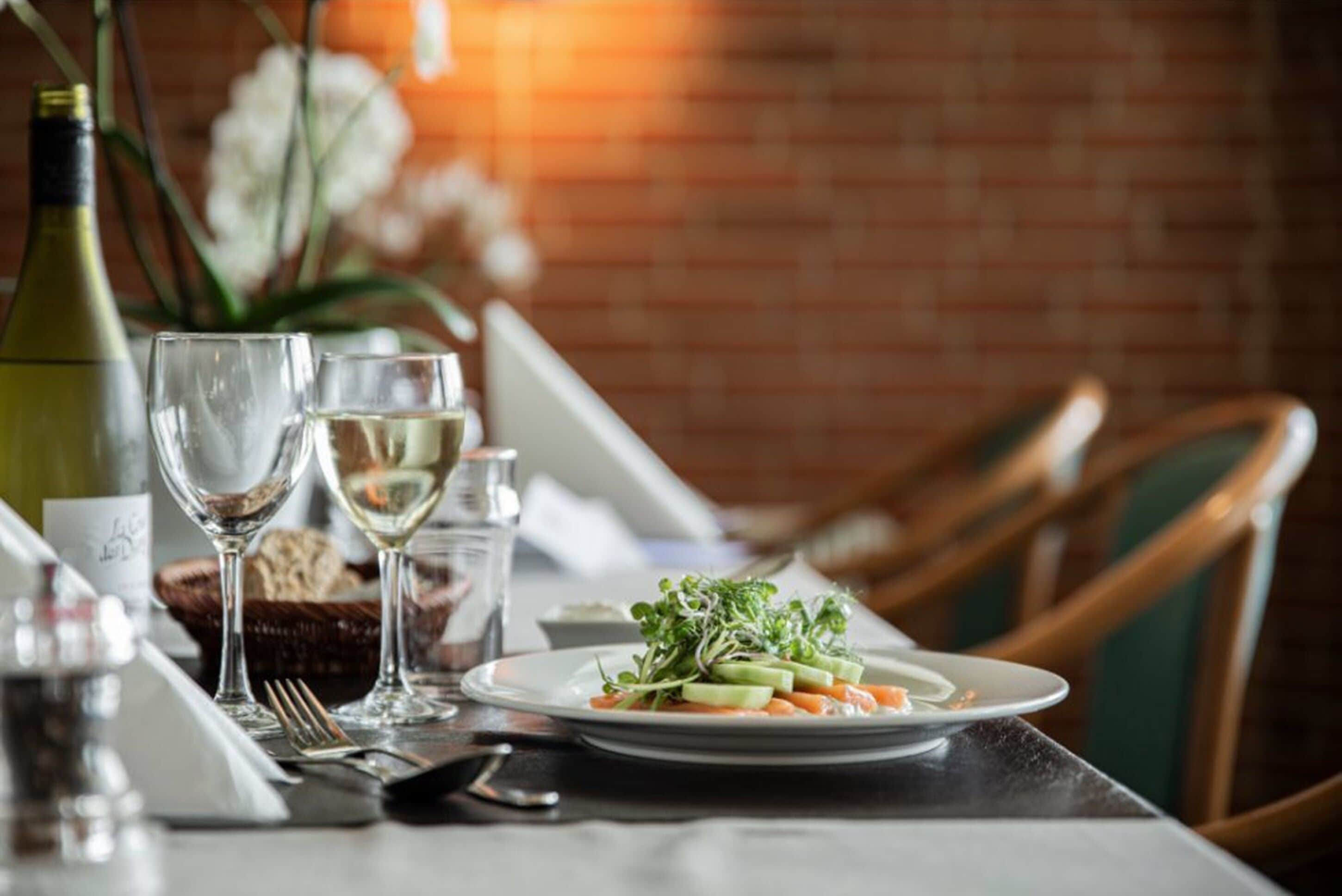 A dining table set with wine glasses, a plate of food, and a bottle of wine.