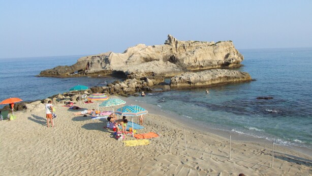 A beach with rocky formations, clear blue water, and umbrellas. - Hotel Damanse (Ricadi)