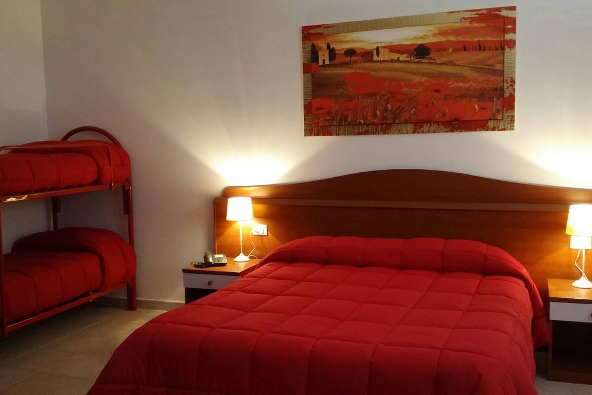A hotel room with a single bed, two bedside tables with lamps, a bunk bed, and a painting on the wall.