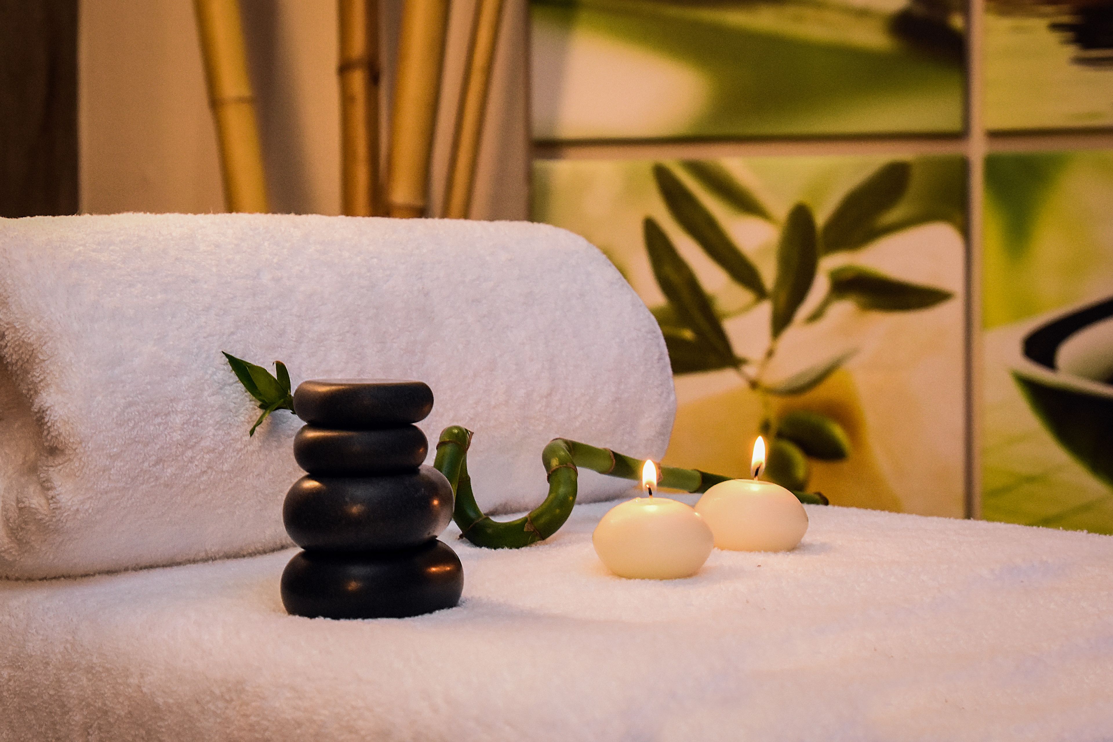 A spa setting with a stack of black stones, two lit candles, and a white towel.