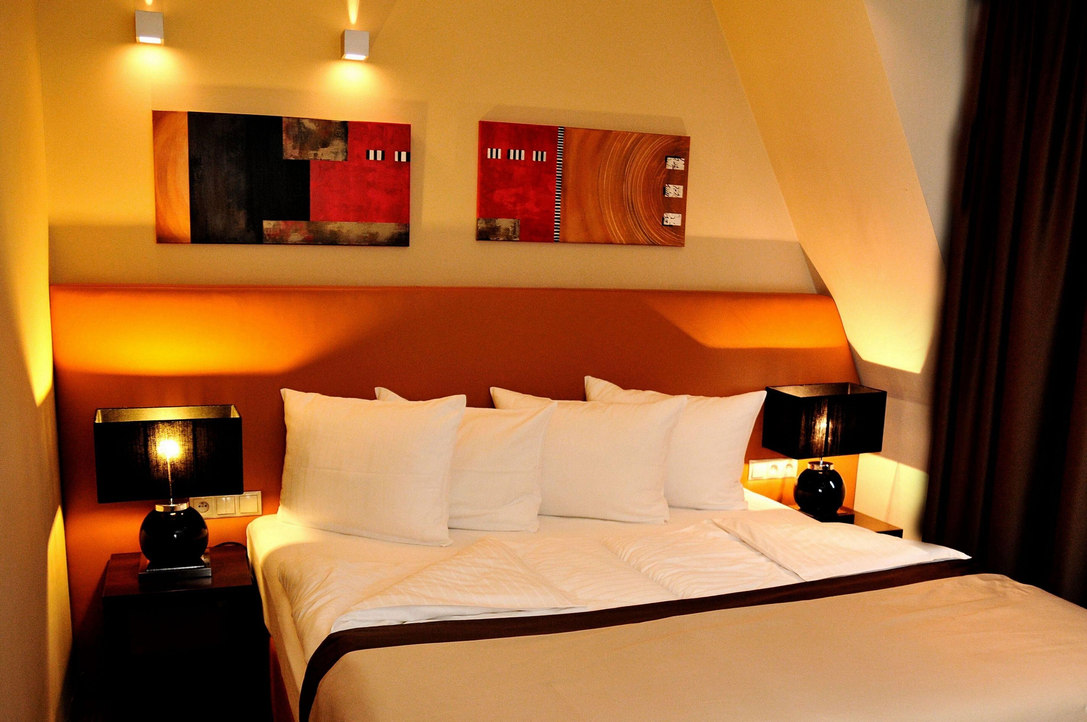 Una habitación de hotel con una cama grande, dos mesitas de noche con lámparas y dos cuadros abstractos en la pared.