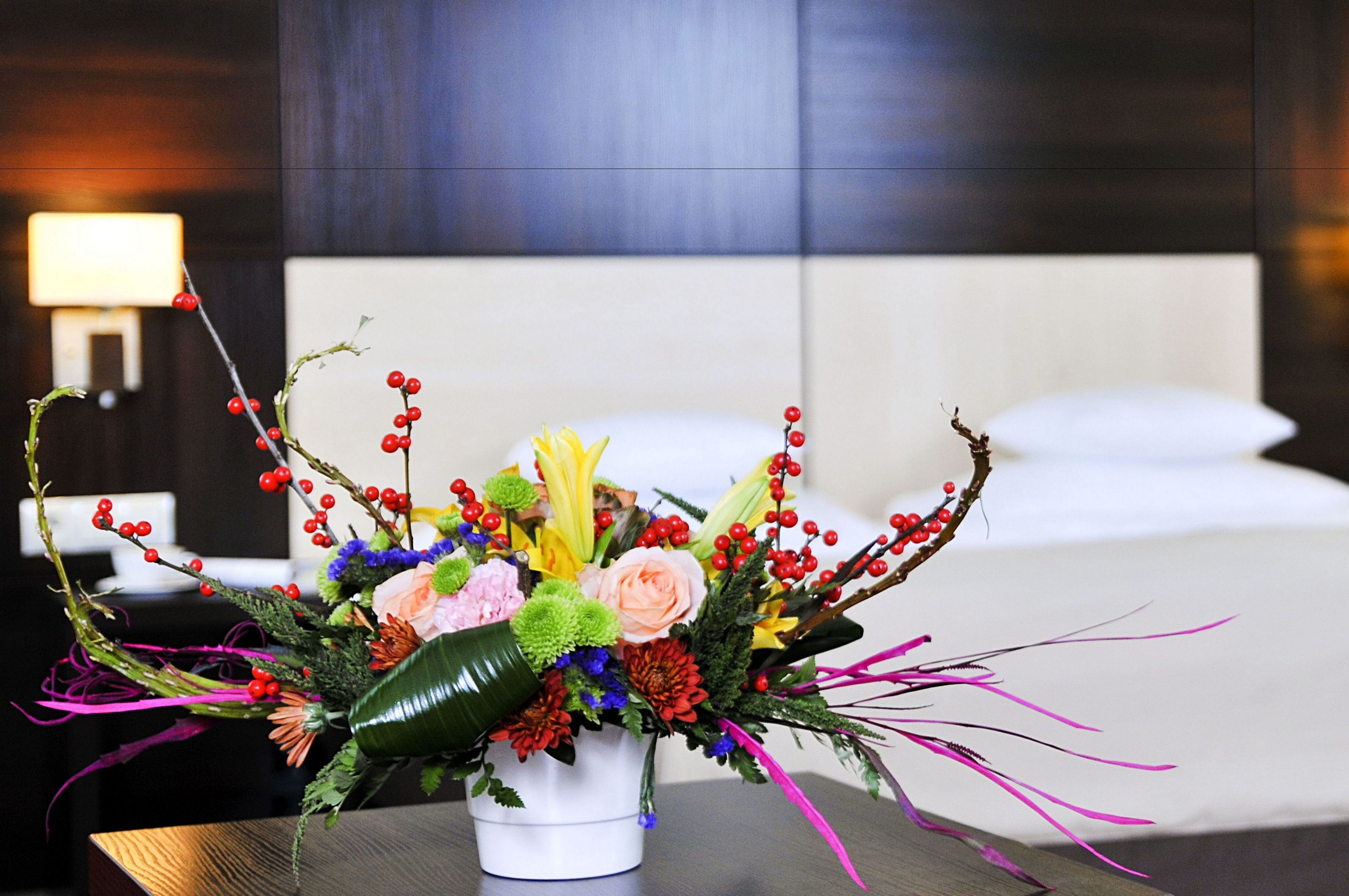 A bouquet of flowers in a white vase on a table in a hotel room.