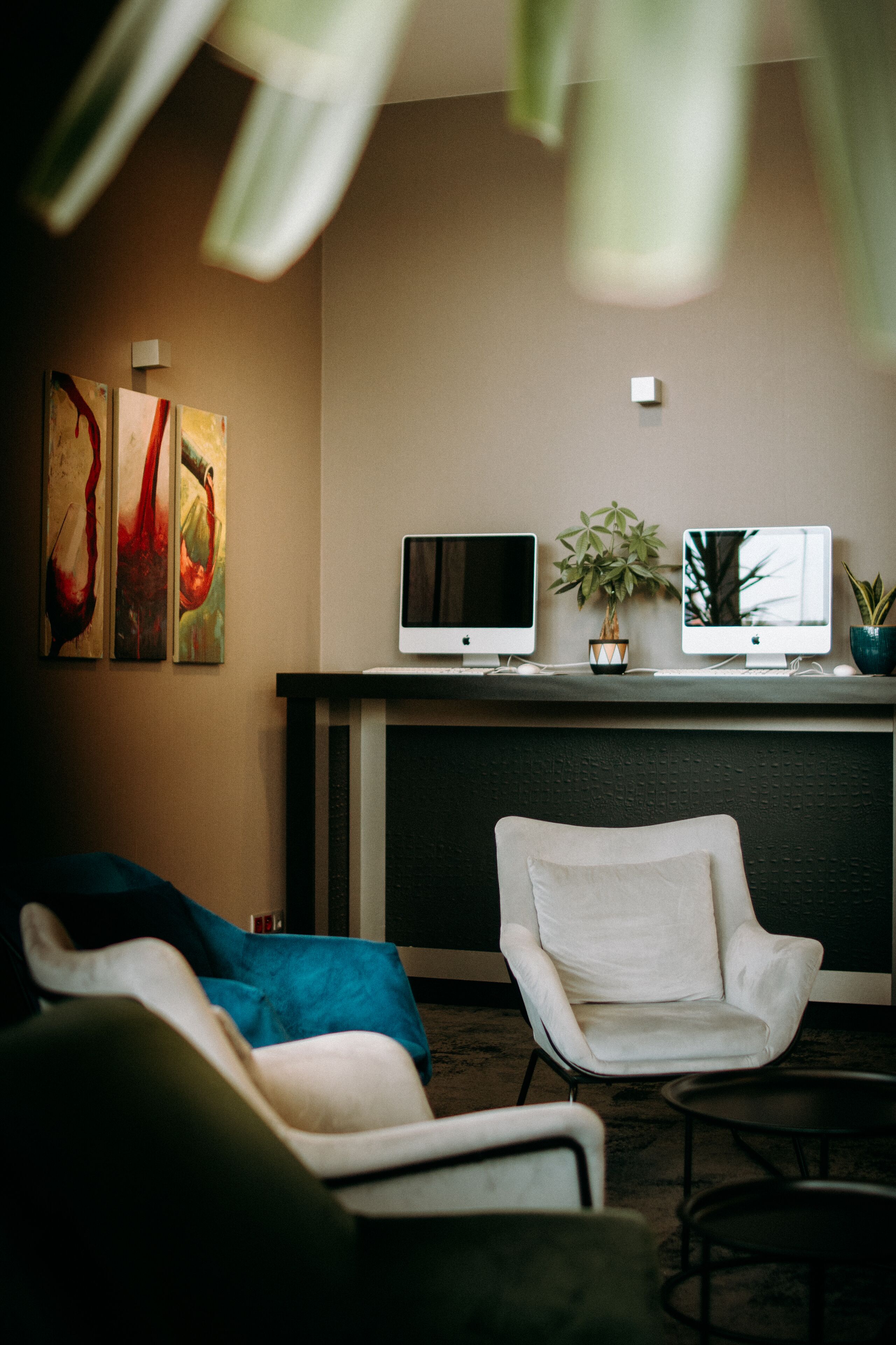 Een moderne woonkamer met twee witte fauteuils, een salontafel en twee flatscreen televisies op een zwarte dressoir. Op de muur hangen abstracte schilderijen en op de dressoir staat een potplant.