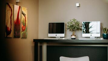 A modern living room with two white armchairs, a coffee table, and two flat-screen TVs on a black console. There are abstract paintings on the wall and a potted plant on the console.