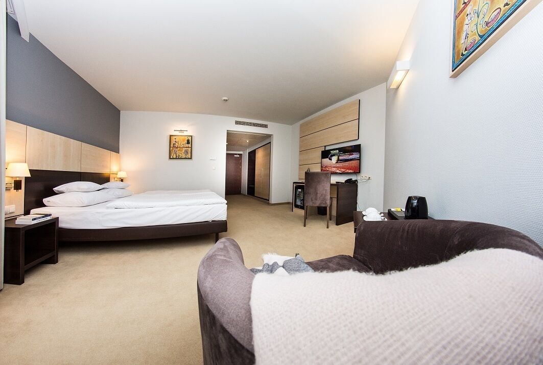 A hotel room with a large bed, a desk, a chair, and a TV.