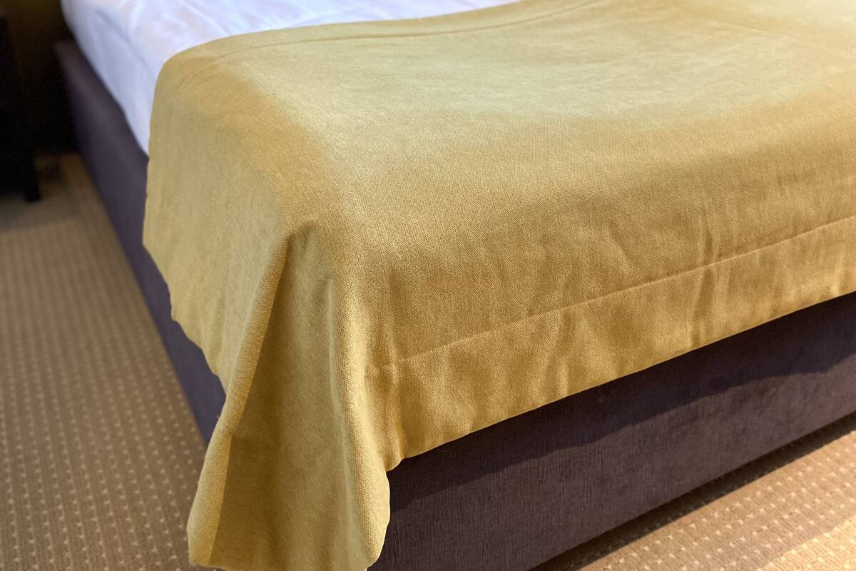 Cama bem arrumada com colcha amarela e travesseiros brancos em um quarto de hotel.