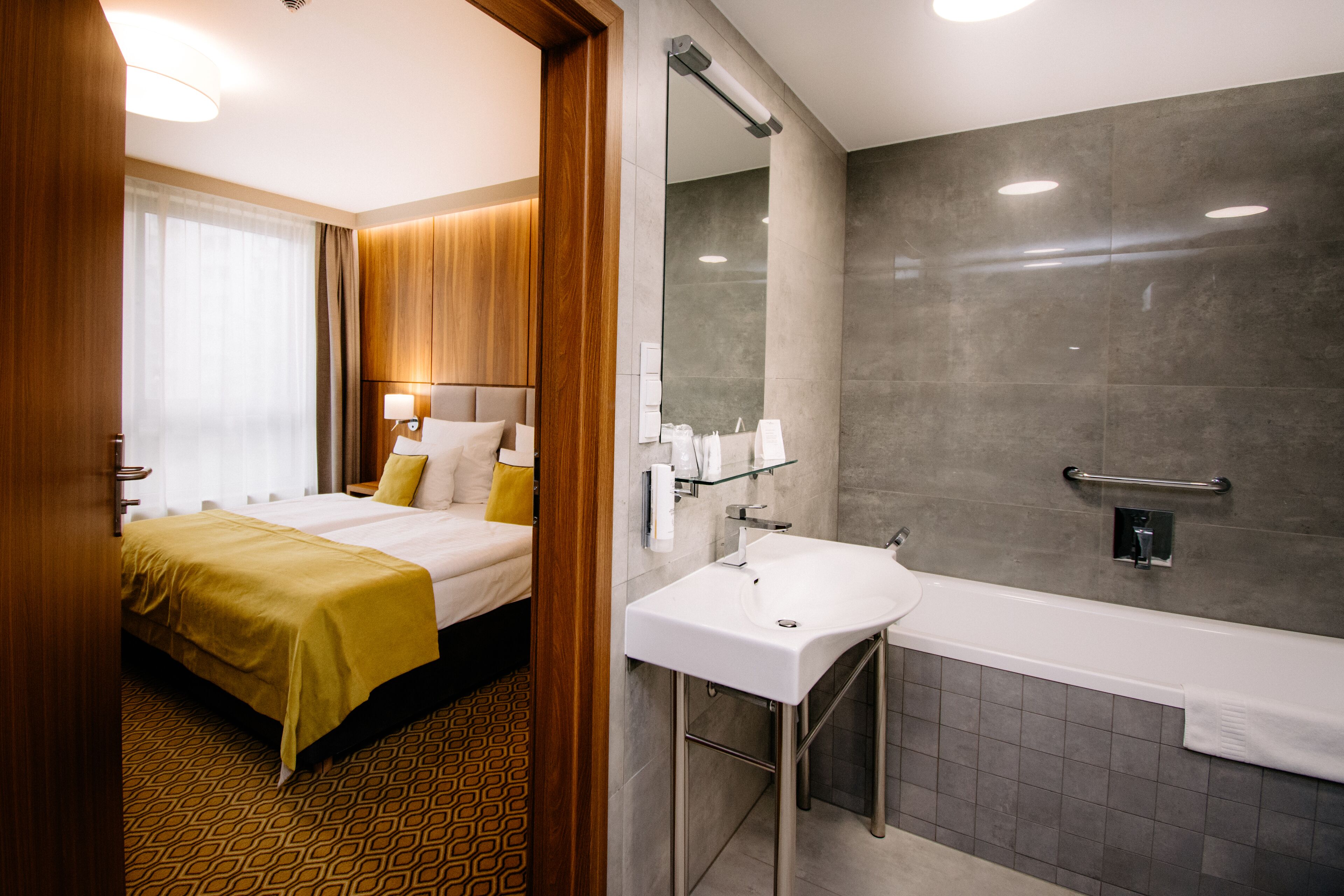 A hotel room with a bed, a bathroom with a sink and mirror, and a shower.